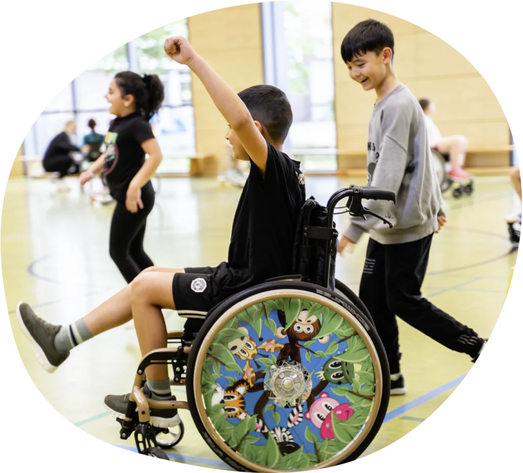 Kind im Rollstuhl auf dem Basketballfeld mit anderen Kindern bei einem Mutmacher Pioniere Workshop